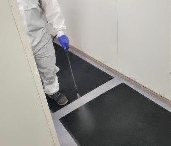 worker in white suit spraying black carpet